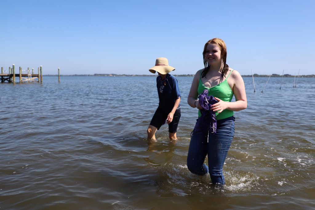 Kaylee Waldon and Aneette Bushnell stand in knee-deep water after having helped release clams into the water. 