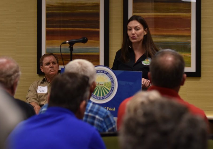 Ag. Commissioner Nikki Fried addresses a hotel conference room full of concerned blueberry growers in Lake City, Florida. Bud Chiles, coordinator of the growers' conference, sits beside her. (Gabriella Paul/ WUFT News)
