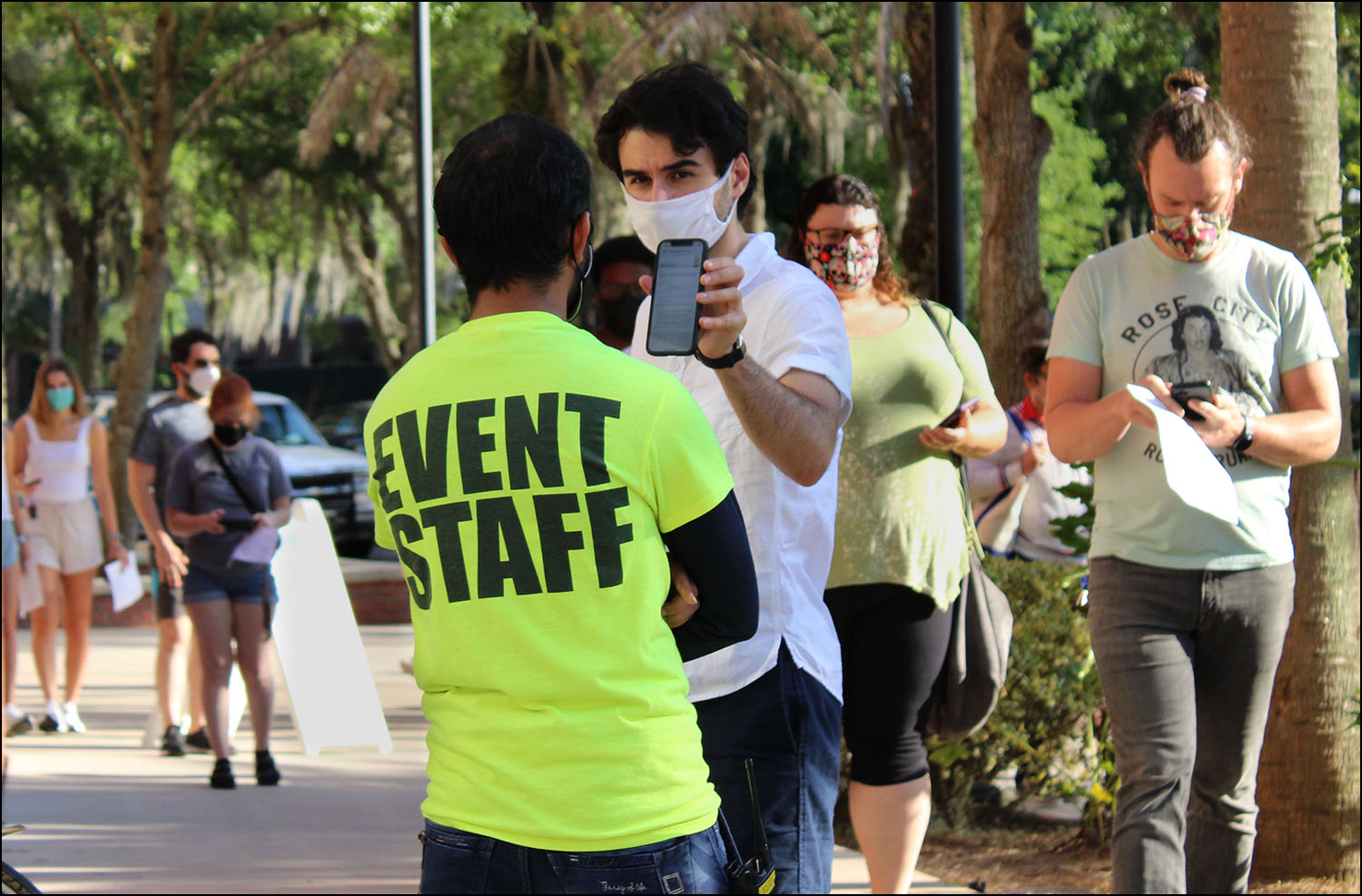People wait in line and show the confirmation page on their phone to the event staff for the COVID-19 vaccine.
