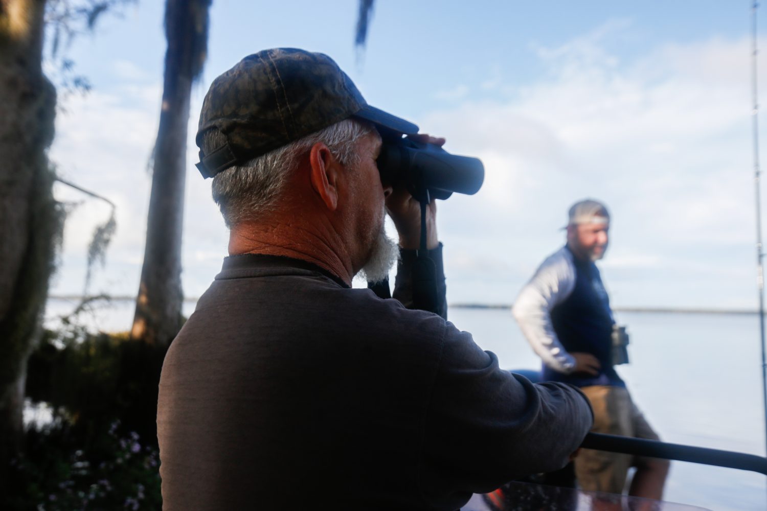Richie Smith looks through binoculars after Alex Horton moved the boat near the shoreline in search of alligators on October 26, 2019. (Chris Day/Fresh Take Florida)