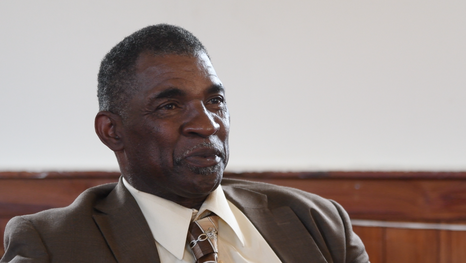 Pastor Harry Joseph sits back in a chair at Mount Triumph Baptist Church in St. James Parish. (Grace King/WUFT News)